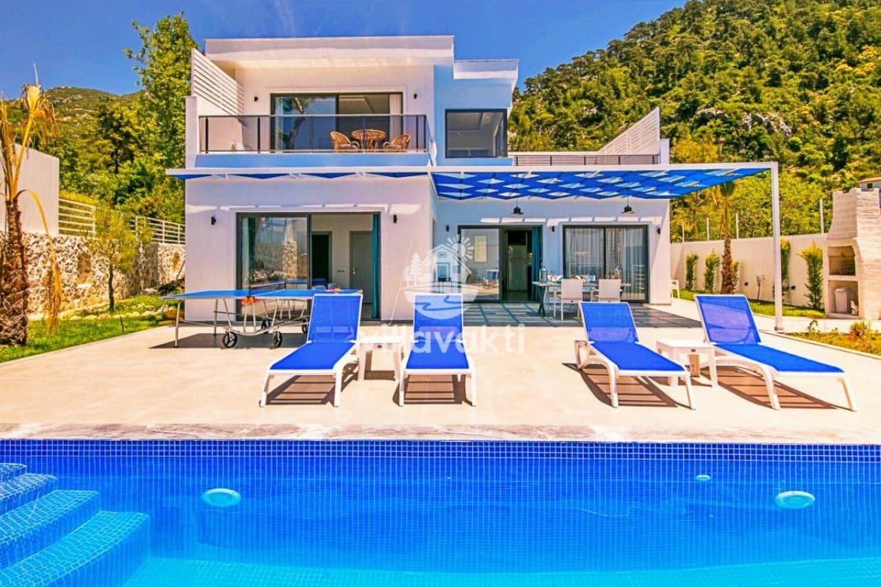 Mavi şezlonglu havuz kenarında beyaz villa ve dağ manzarası