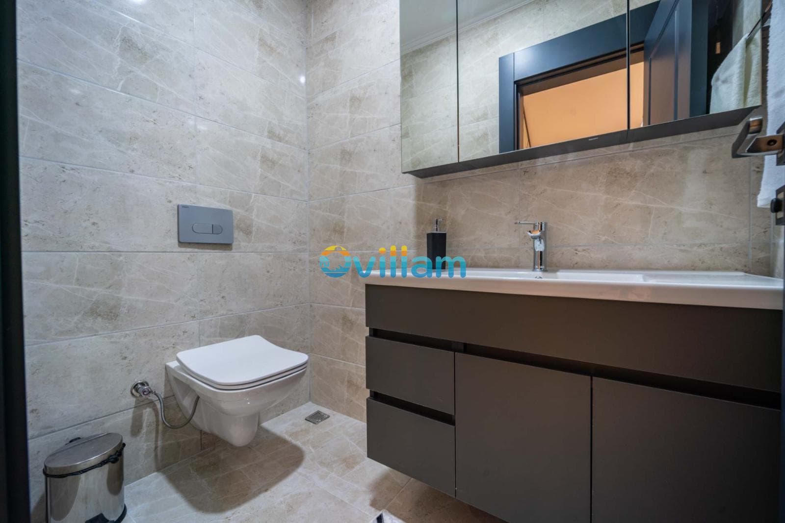 Bej seramik kaplı modern banyoda klozet ve aynalı lavabo ünitesi.