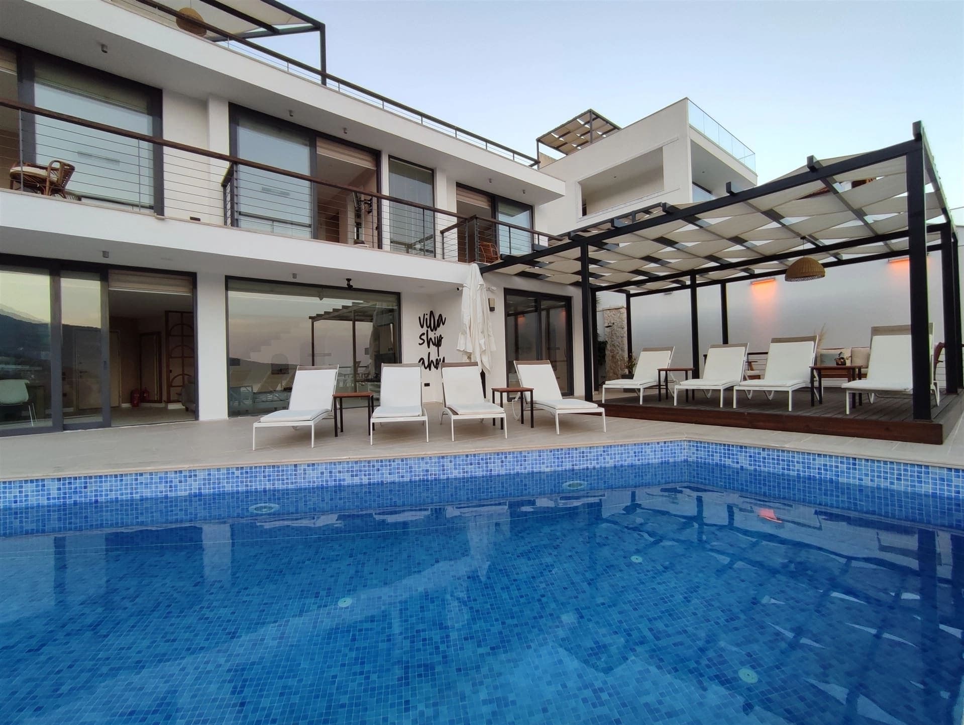 Önünde havuz ve şezlonglar bulunan modern villanın dış cephesi.