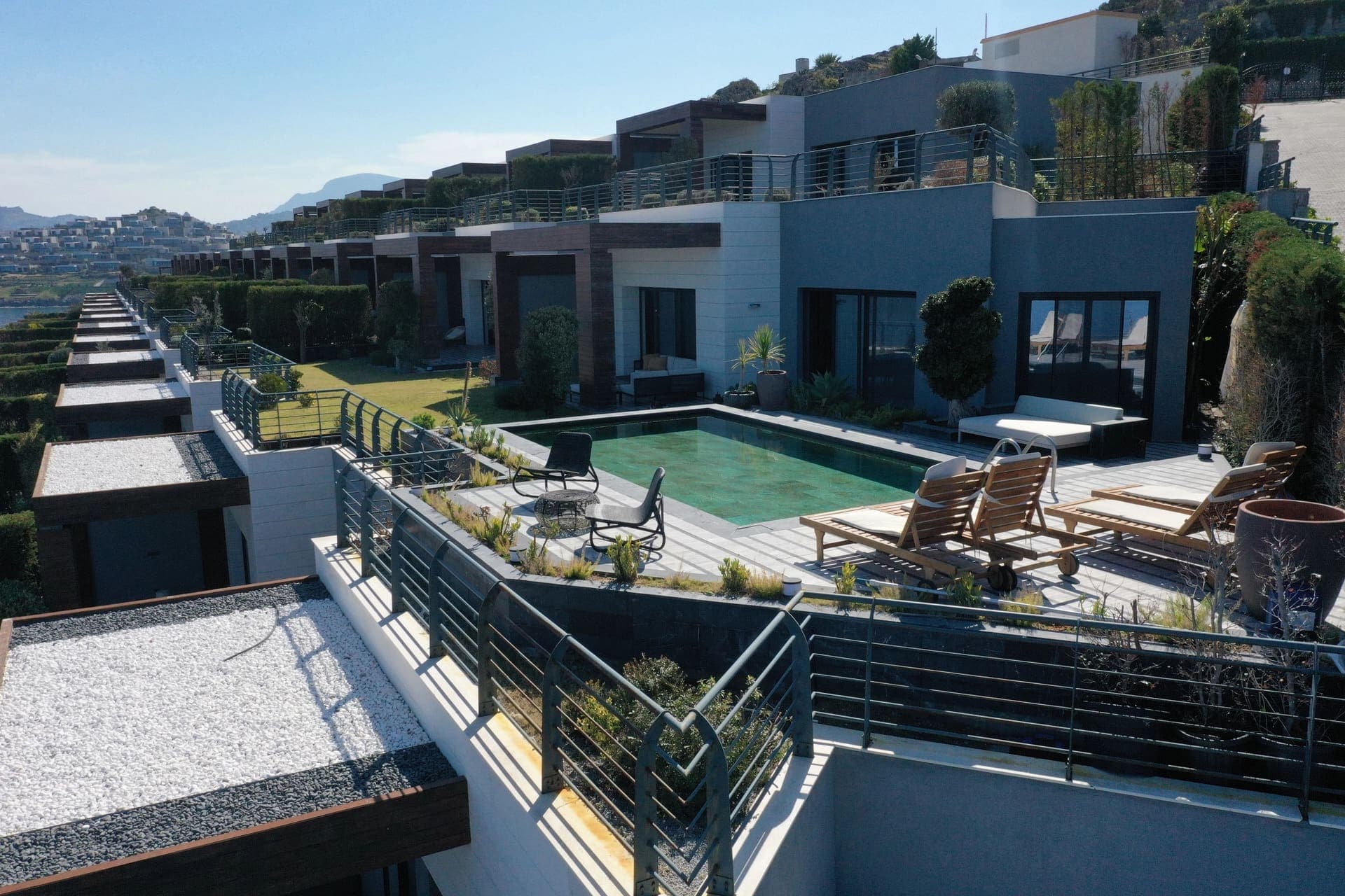 Kademeli modern villa bloklarının önünde özel havuz ve şezlonglar var.