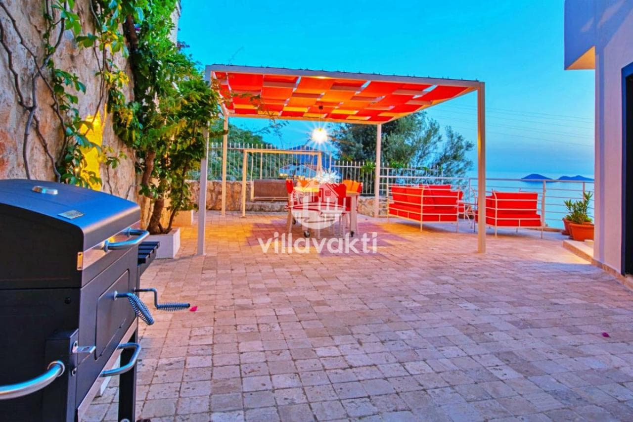 Kırmızı minderli oturma grubu ve barbekü bulunan taş zeminli veranda.