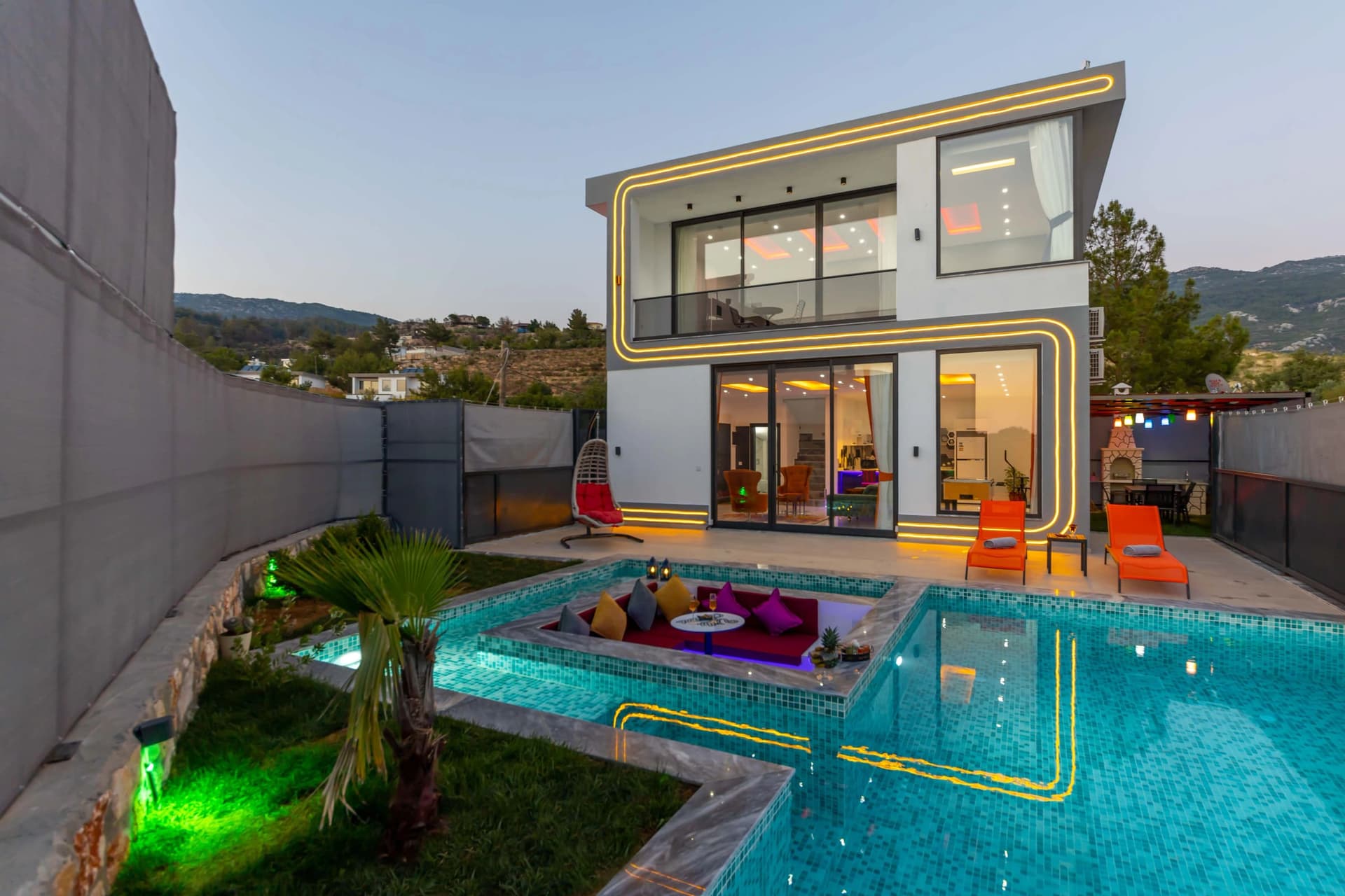 Havuz ortasında oturma alanı ve şezlonglar bulunan modern villanın dış görünümü.