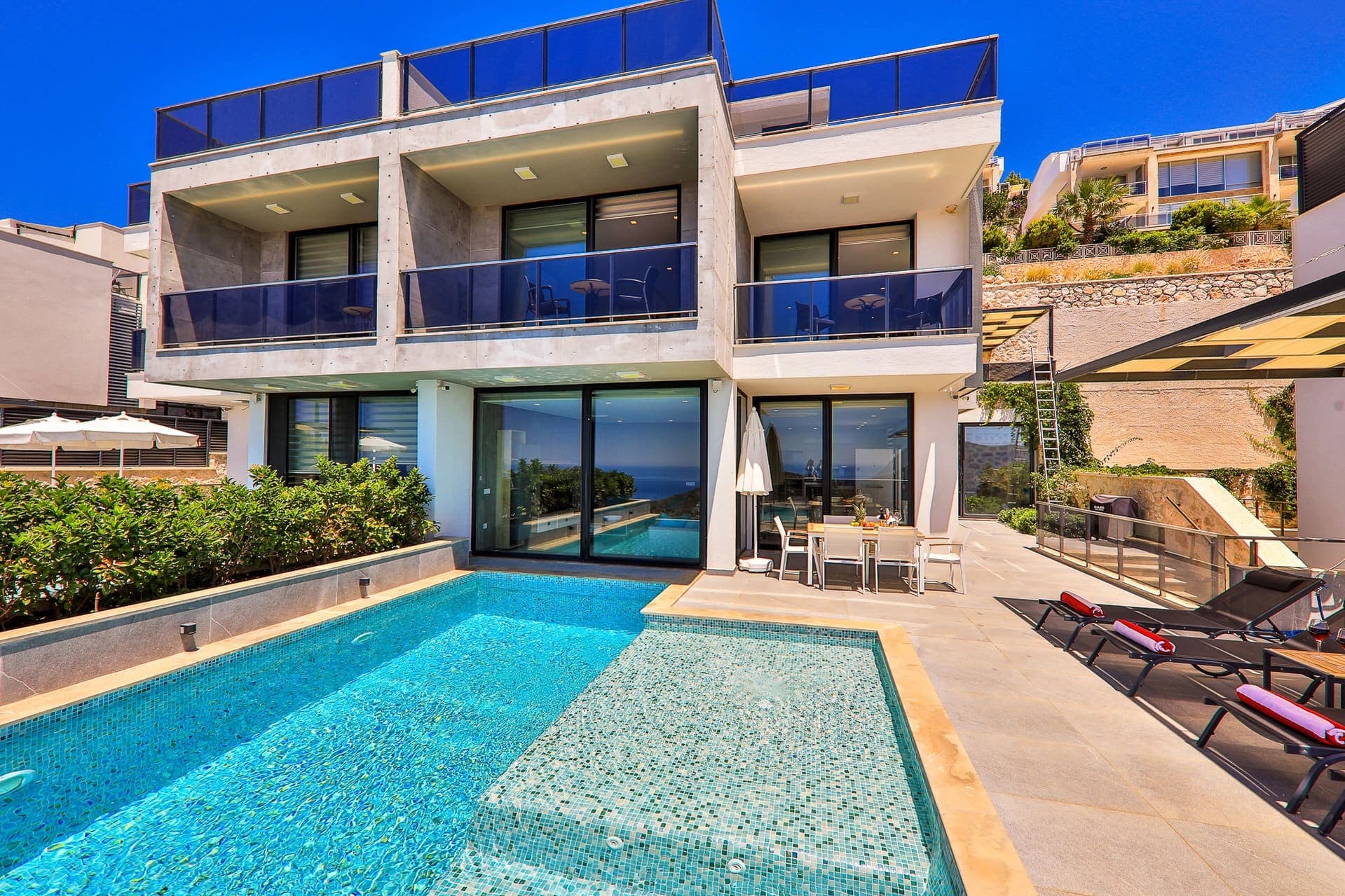 Önünde havuzu, şezlongları ve yemek masası bulunan iki katlı modern villa