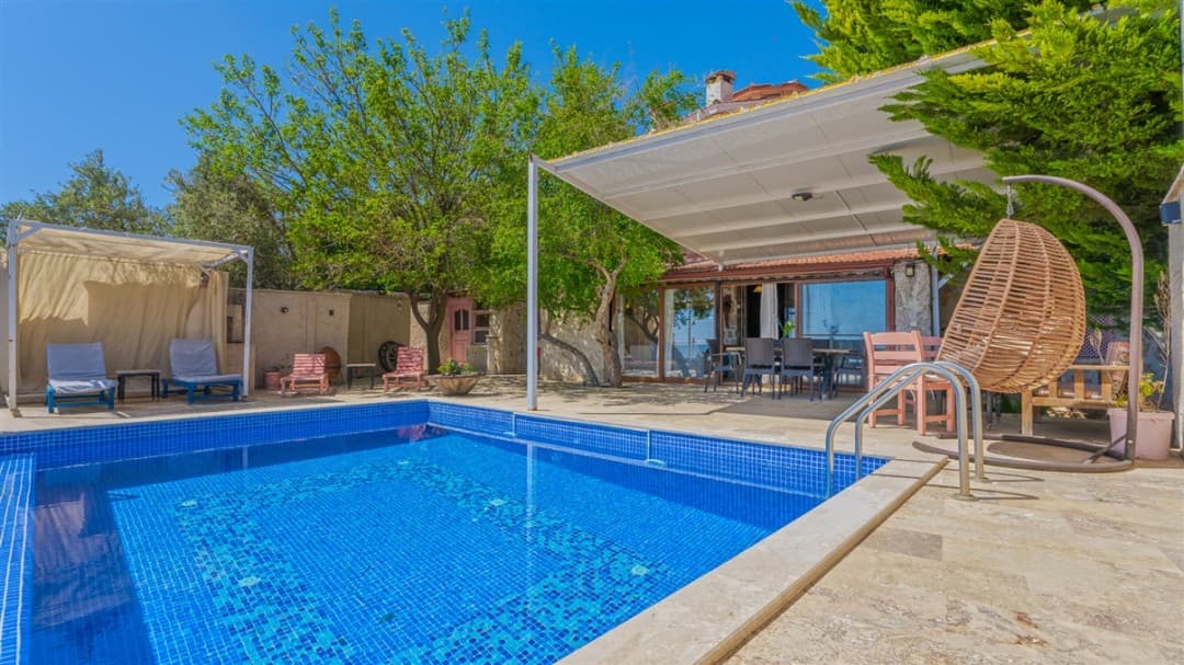 Mavi yüzme havuzlu ve gölgelikli oturma alanı bulunan villa bahçesi.