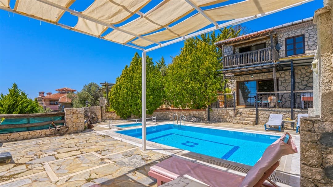 Güneşli günde havuzlu ve taş duvarlı iki katlı villa bahçesi.