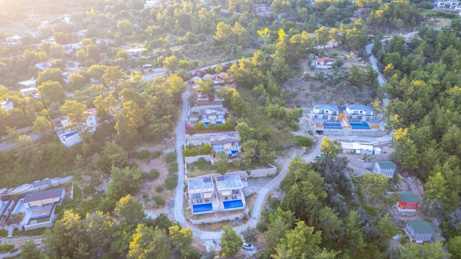Ormanlık alandaki villaların ve aralarındaki yolun havadan görünümü.