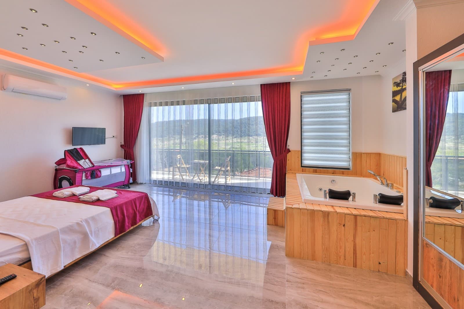 Kırmızı perdeli yatak odasında ahşap kaplamalı jakuzi ve geniş cam balkon.