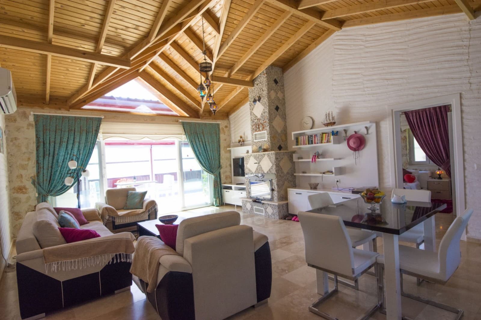 Ahşap tavanlı geniş salon, oturma grubu ve yemek masası.