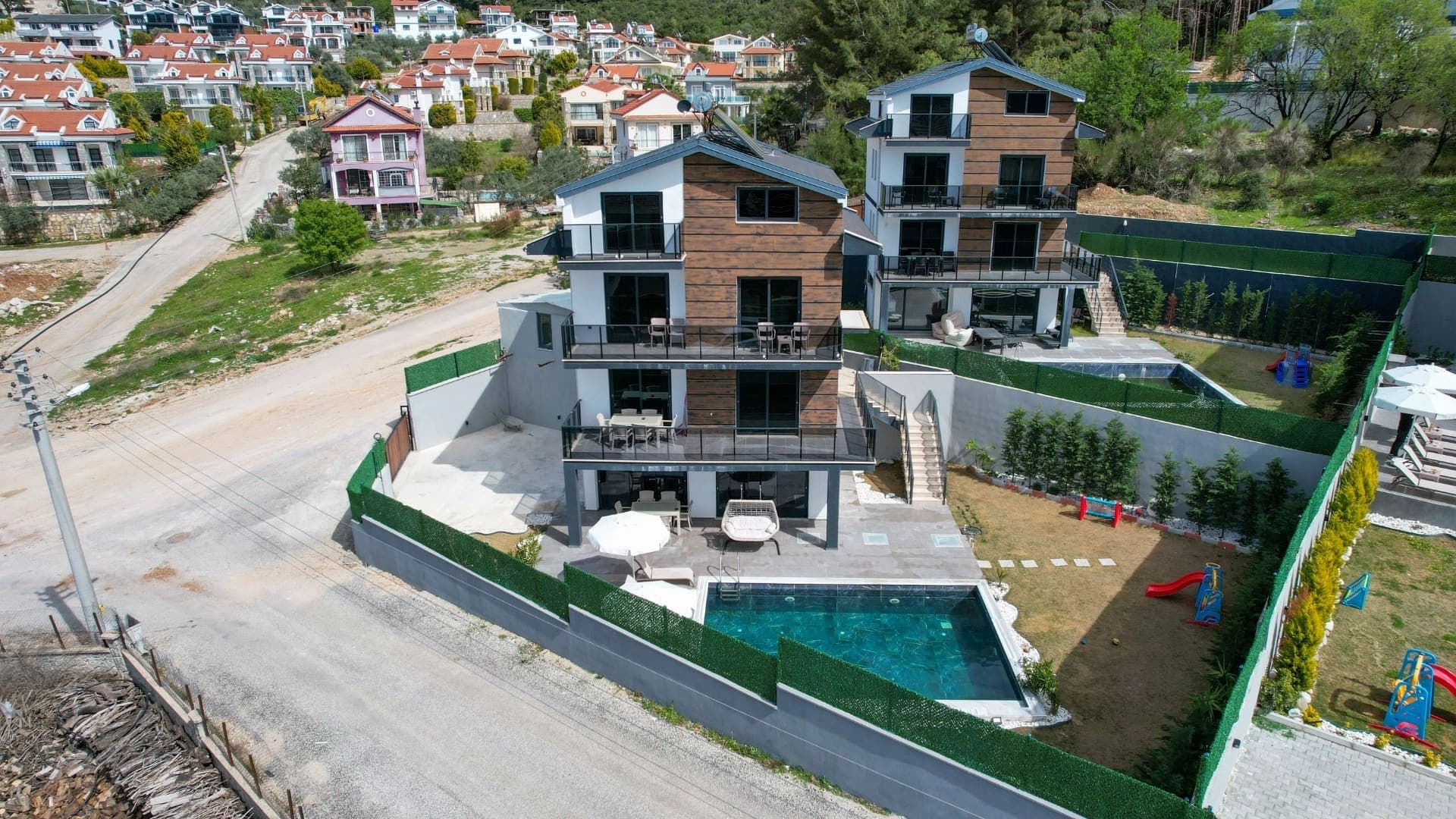 Yüksekten çekilen havadan görünümde havuzlu ve bahçeli yan yana villalar.