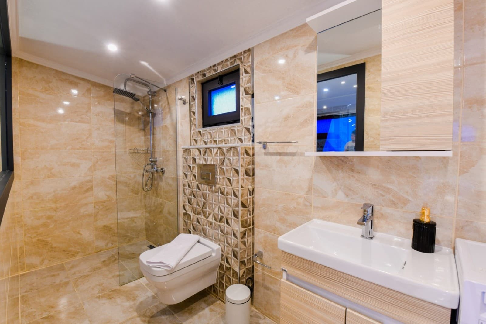 Bej seramik kaplı duvarları olan, duşakabin ve asma lavabolu banyo.