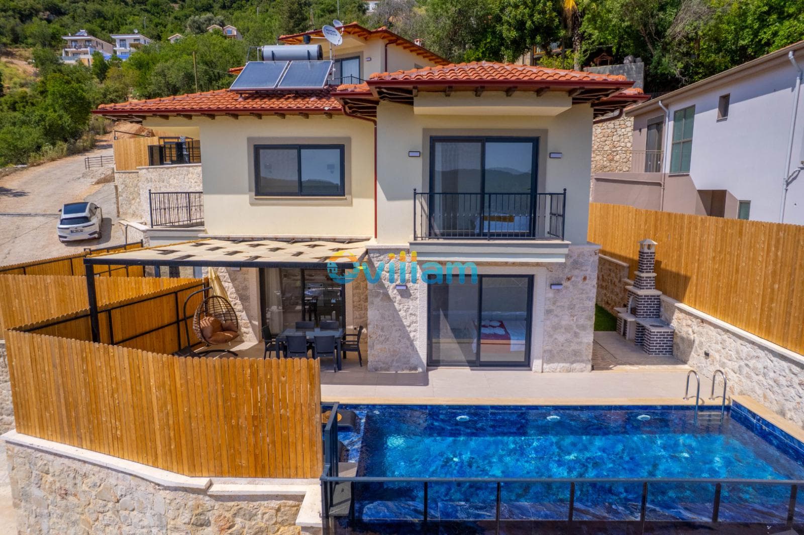 Ahşap çitlerle çevrili bahçesinde havuz ve güneşlenme alanı bulunan kiremit çatılı iki katlı villa.