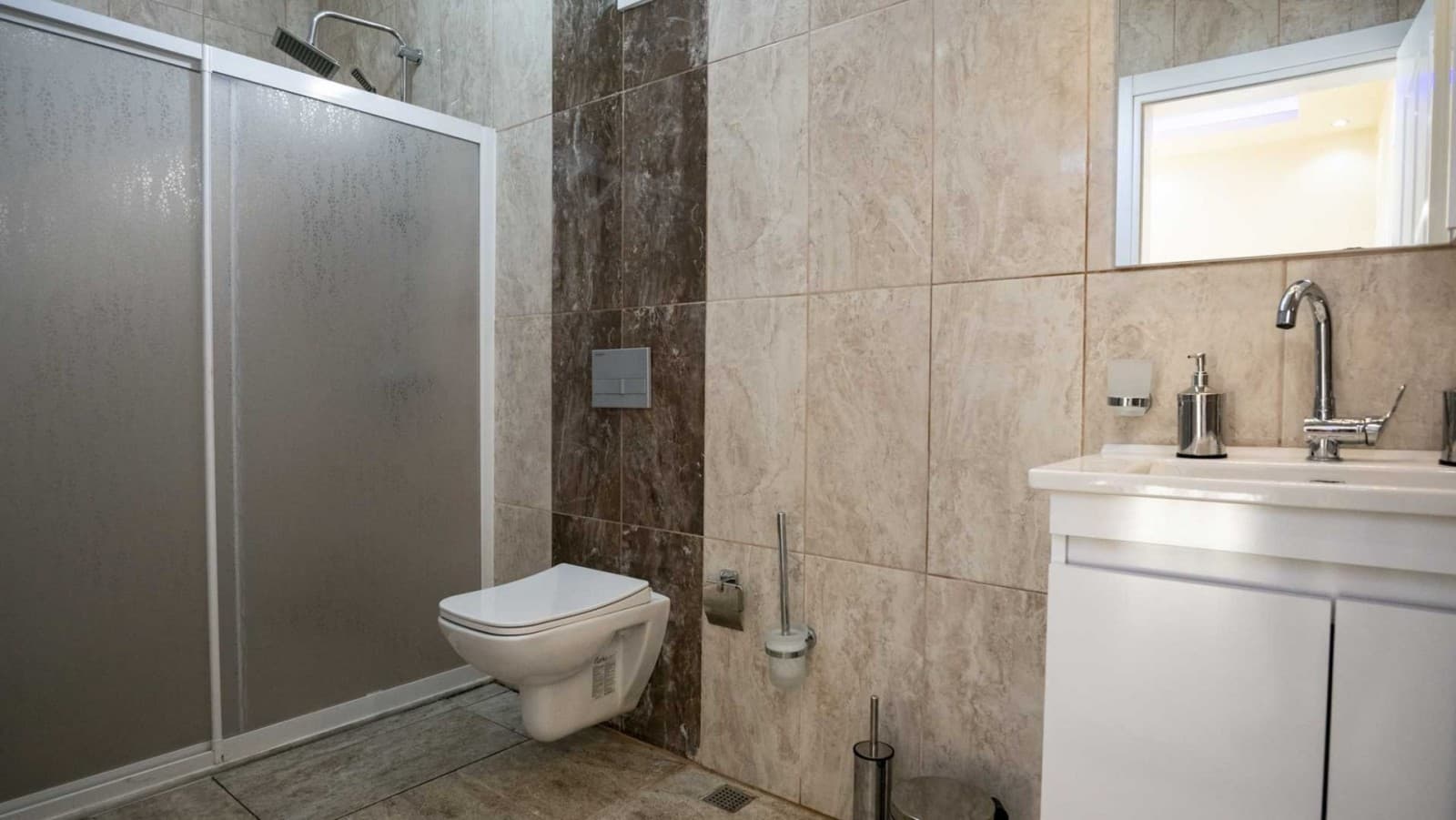 Kahverengi ve bej tonlarında seramik kaplı duvarları olan duşakabinli banyo.