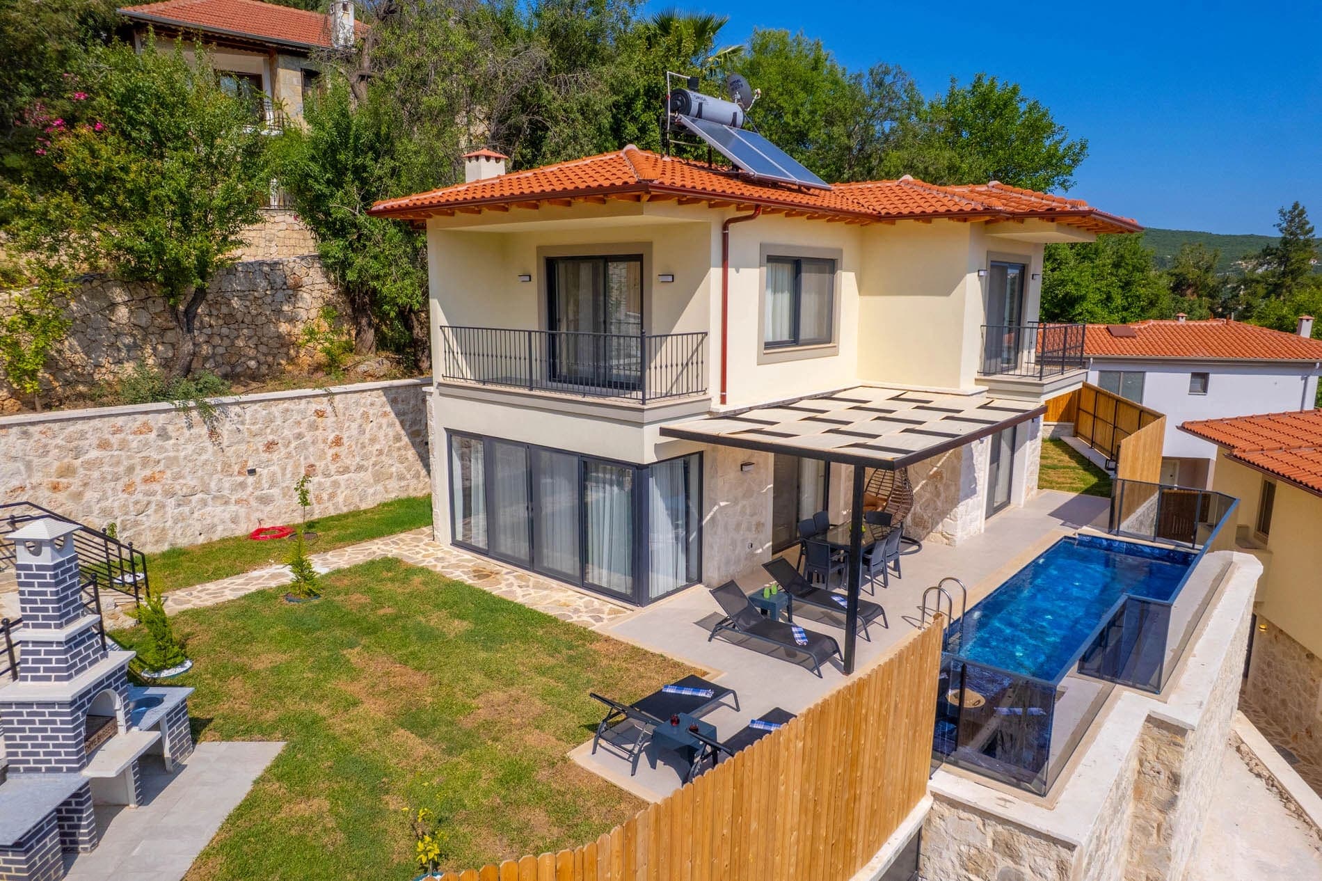Ahşap çitli bahçesi, havuzu, şezlongları ve tuğla barbeküsü olan müstakil villa.