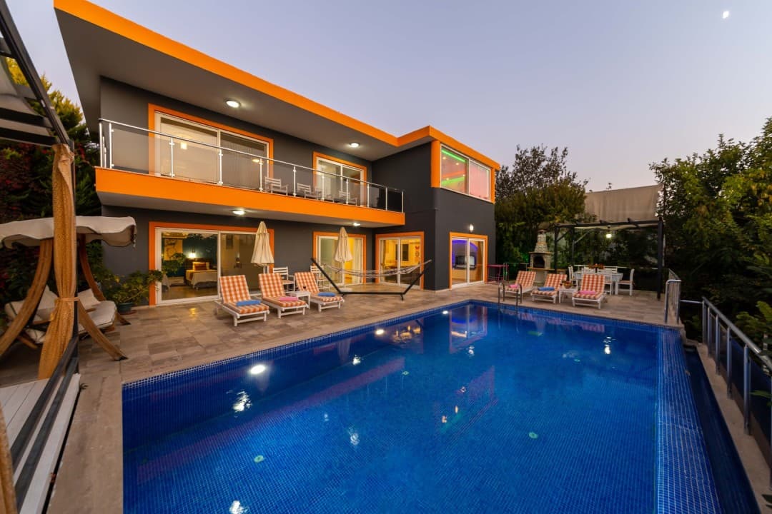 Akşam ışıklarında turuncu detaylı iki katlı villa ve havuzu.