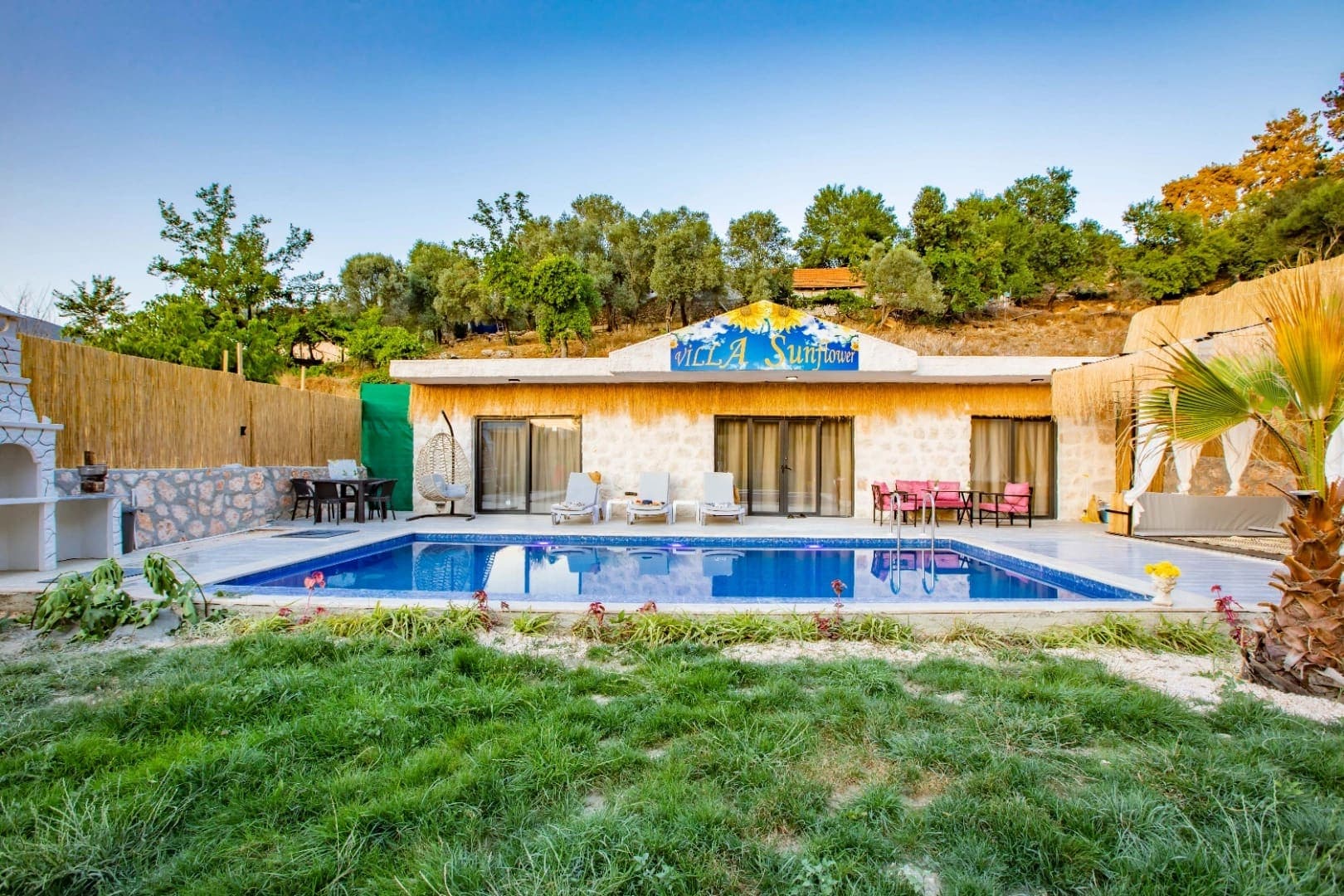 Villa Sunflower tabelalı tek katlı taş evin önünde havuz ve şezlonglar.
