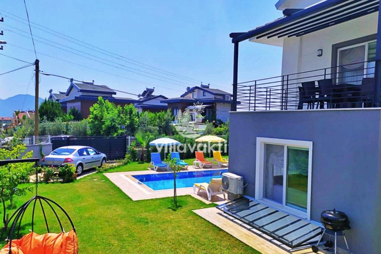 Müstakil villanın bahçesinde dikdörtgen havuz, şezlonglar, güneş şemsiyeleri ve barbekü alanı bulunuyor.