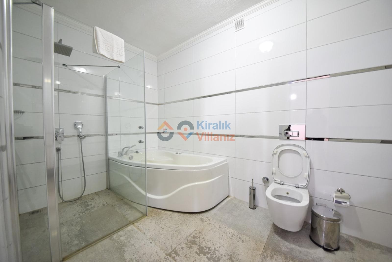 Beyaz fayanslı banyoda cam kabinli duş alanı, jakuzi ve asma klozet.