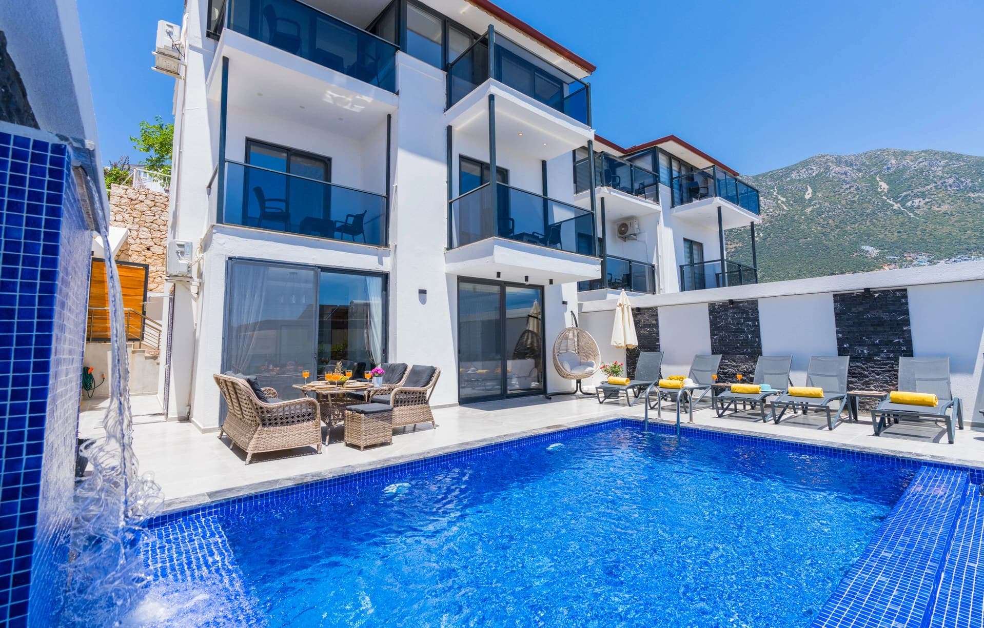Önünde havuz, şezlonglar ve oturma grubu bulunan beyaz dış cepheli katlı villa.