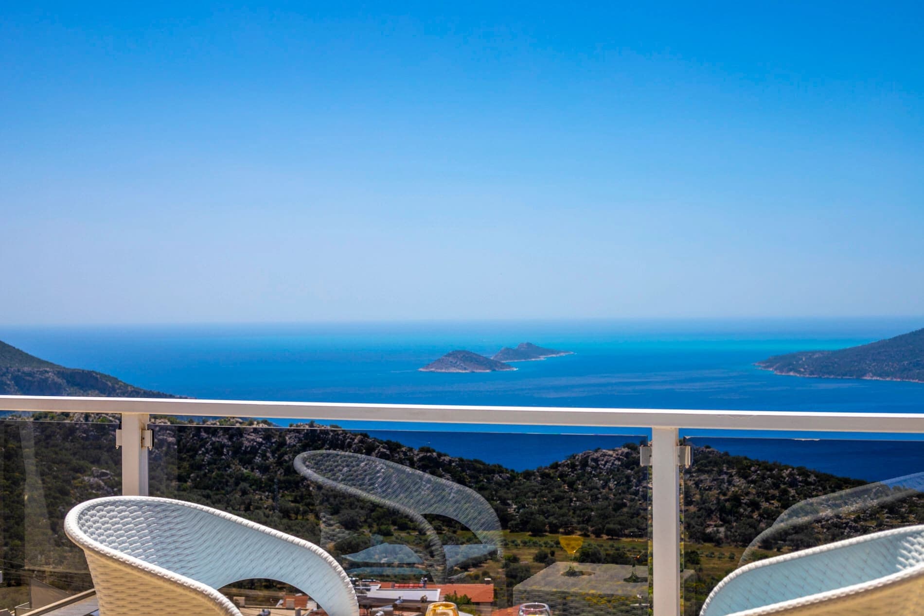 Balkondan görünen deniz, adalar ve yeşil tepeler manzarası.