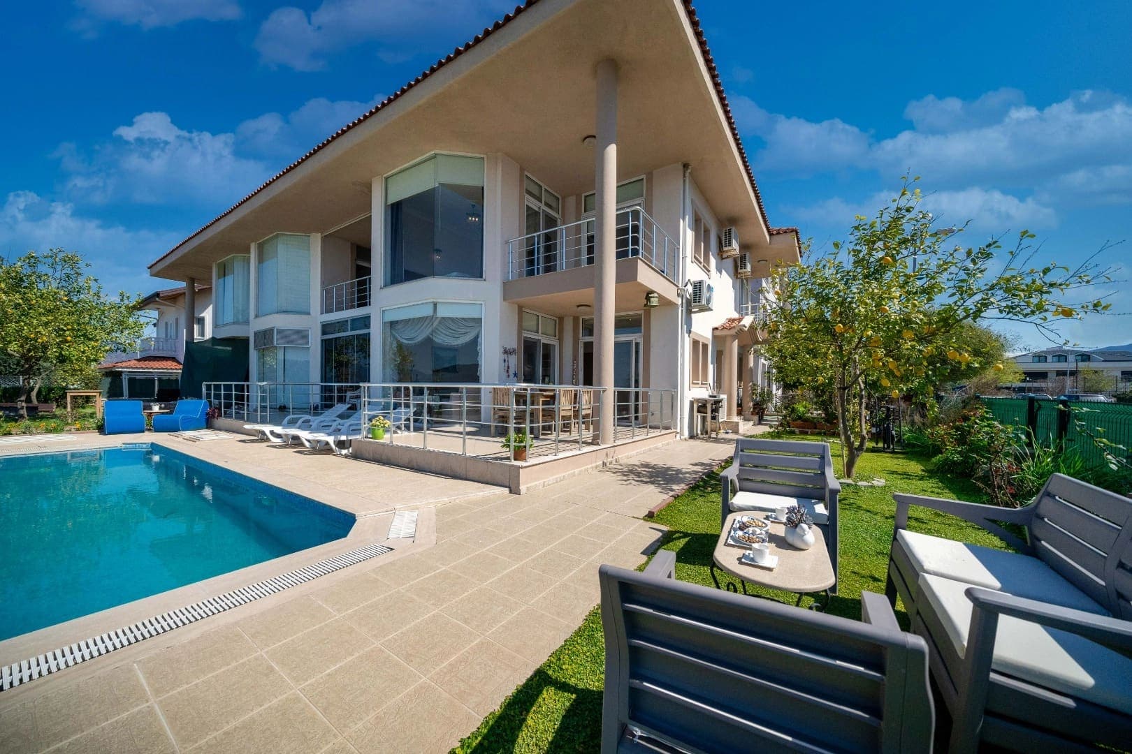 Bahçesinde havuz, şezlonglar ve oturma grubu olan iki katlı modern villa.