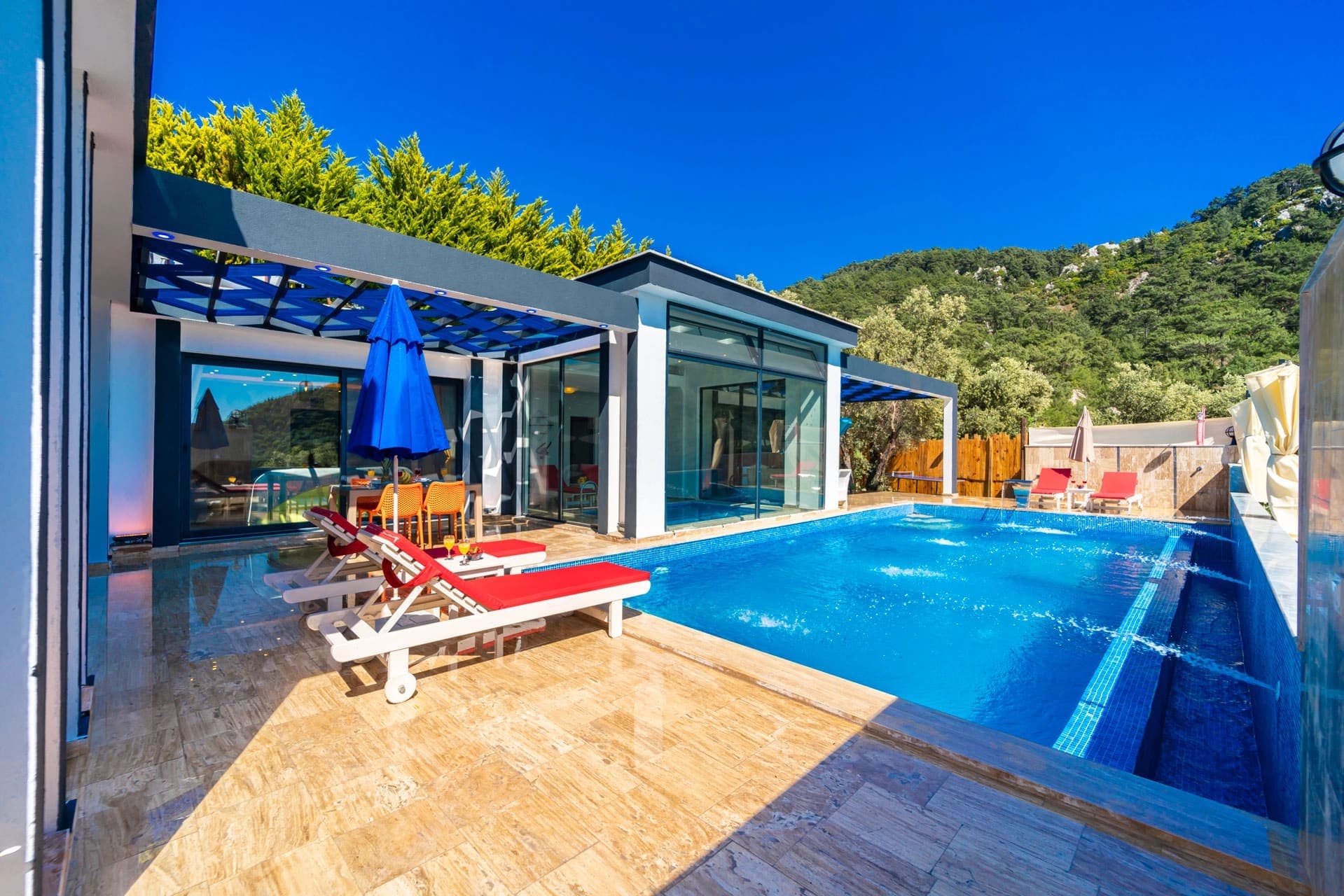 Mavi havuz, kırmızı şezlonglar ve şemsiyelerle döşenmiş modern villa terası.