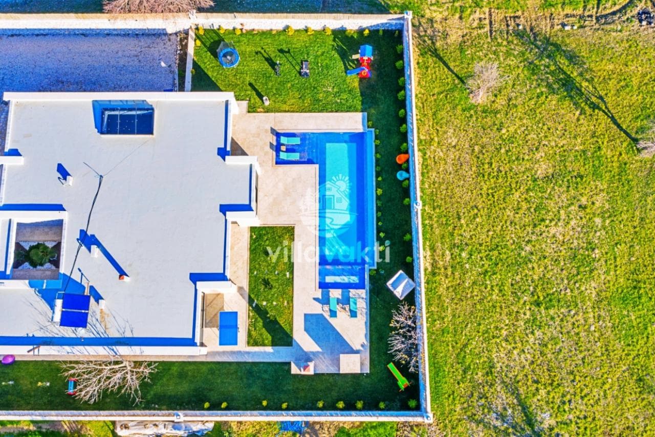 Villa ve bahçesinin kuş bakışı görünümü, dikdörtgen havuz ve yeşil alan.