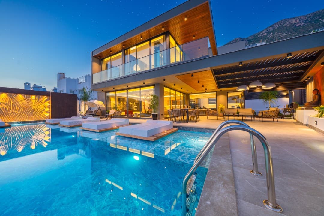 Gece vakti ışıklandırılmış havuz ve havuz içi yatakları olan modern villanın dış cephesi.