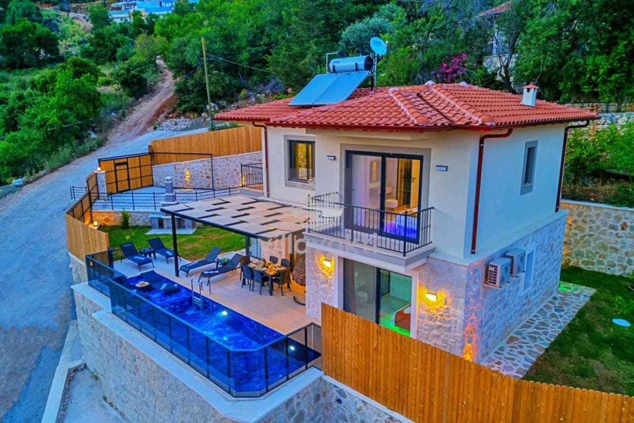 Yamaçta konumlanmış, kiremit çatılı, özel havuzlu ve ahşap çitlerle çevrili bahçeli villa.