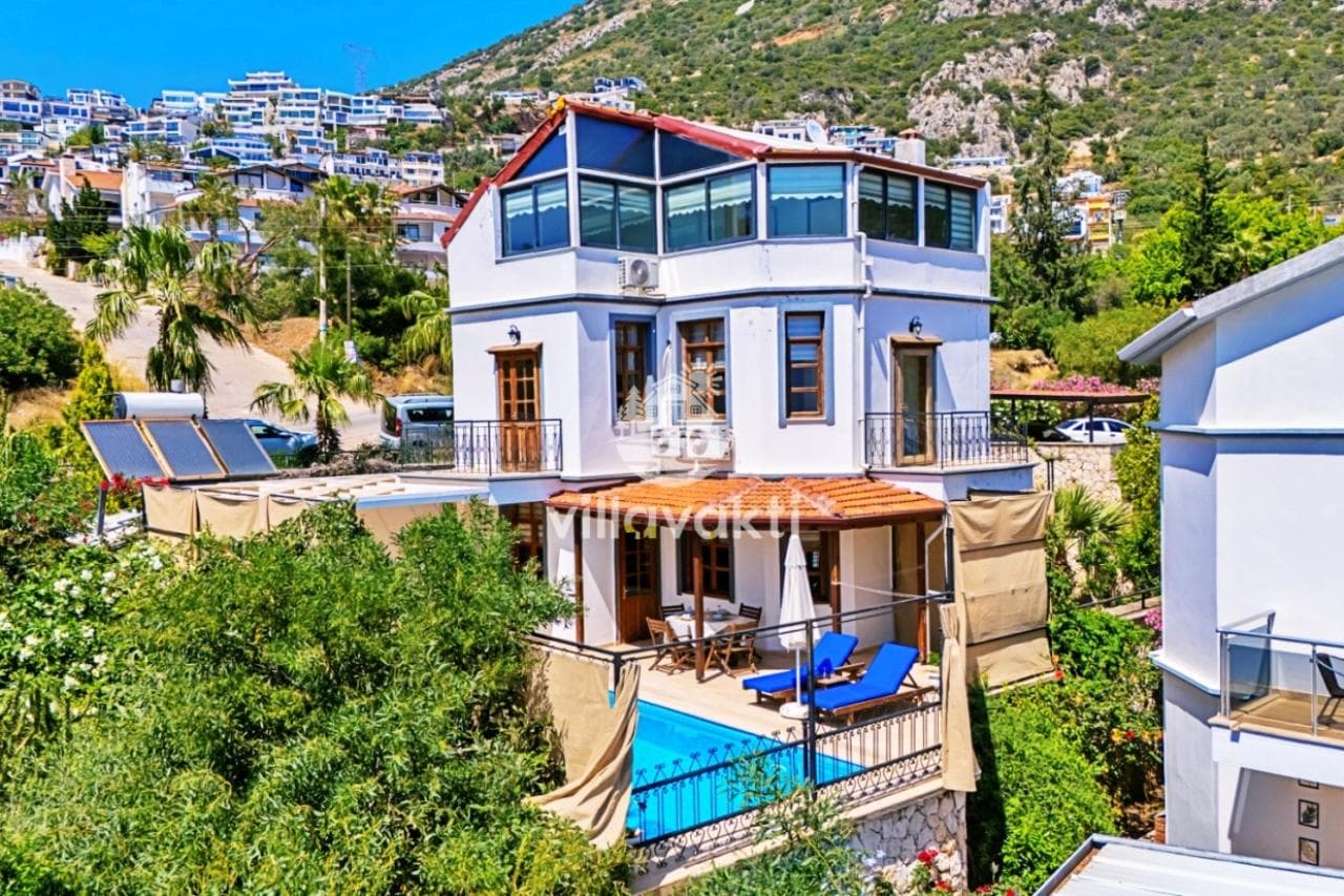 Yamaçtaki yerleşim içinde, teraslı, havuzlu ve beyaz dış cepheli üç katlı villa.