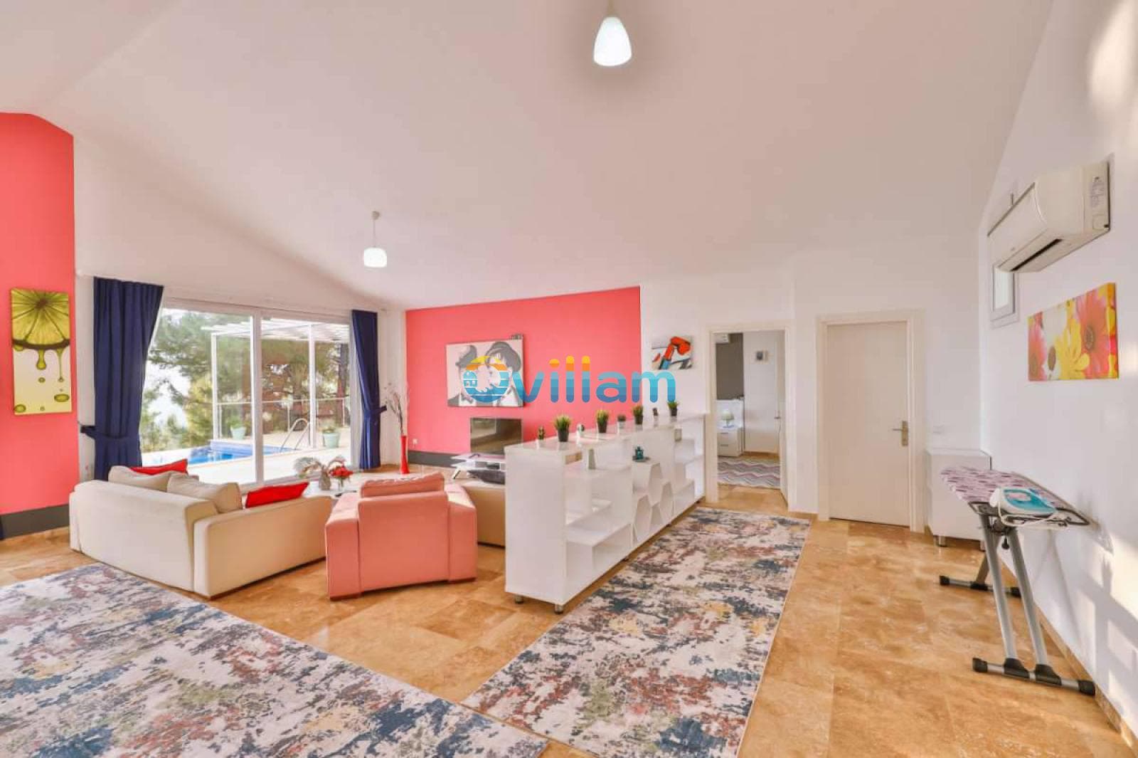 Pembe duvarlı ve renkli halılı aydınlık oturma odasından havuz manzarası.