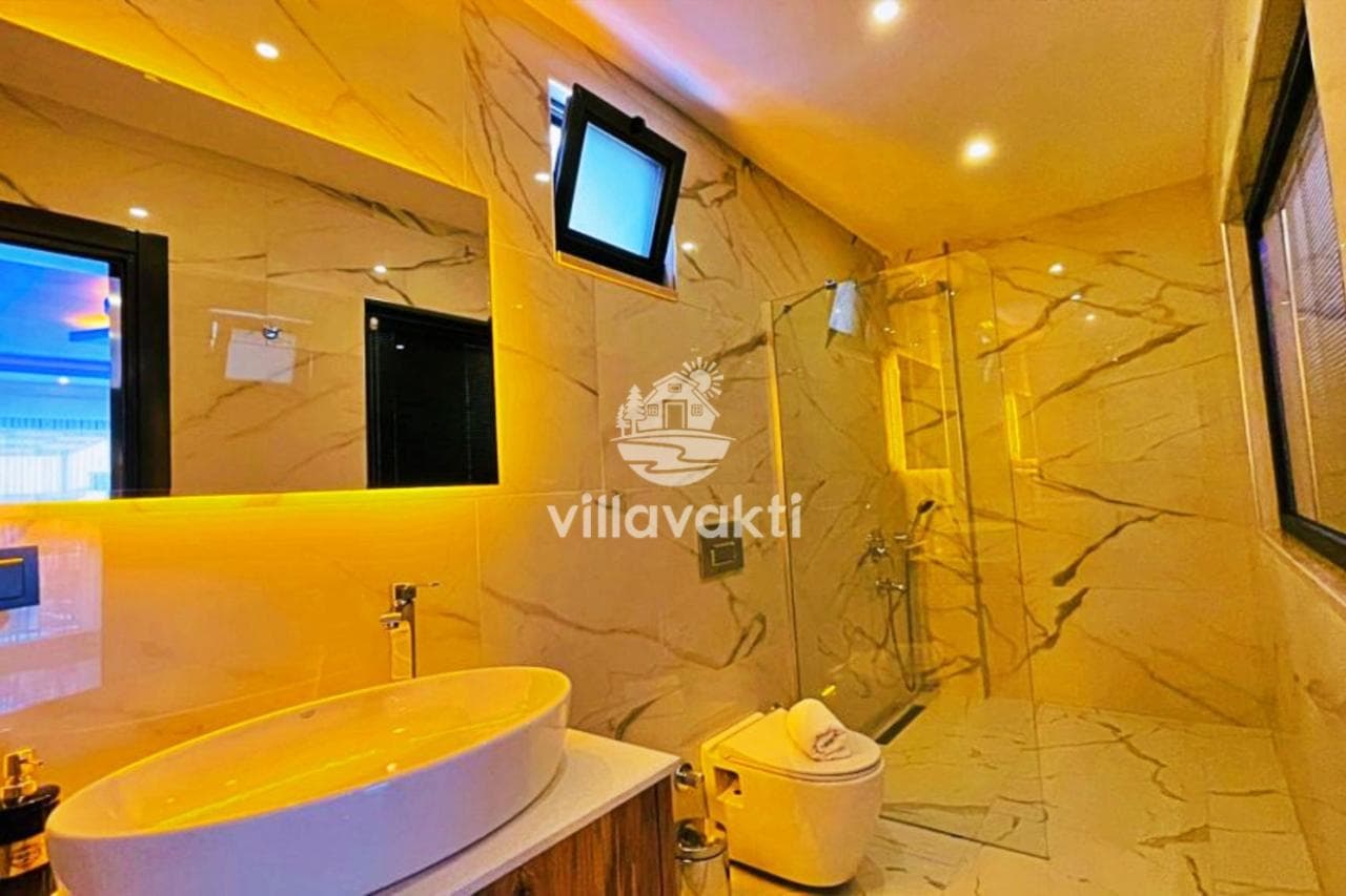 Mermer kaplı duvarlara sahip, duşakabinli ve şık aydınlatmalı banyo.