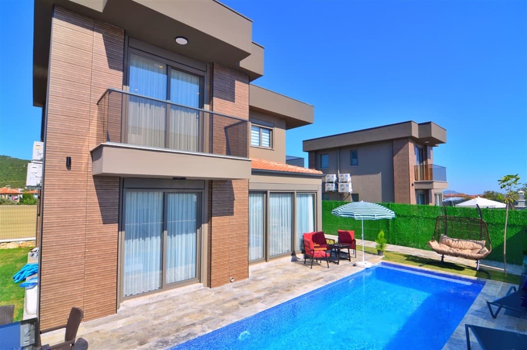 Önünde özel havuzu, şezlongları ve oturma alanı bulunan modern dış cepheli iki katlı villa.