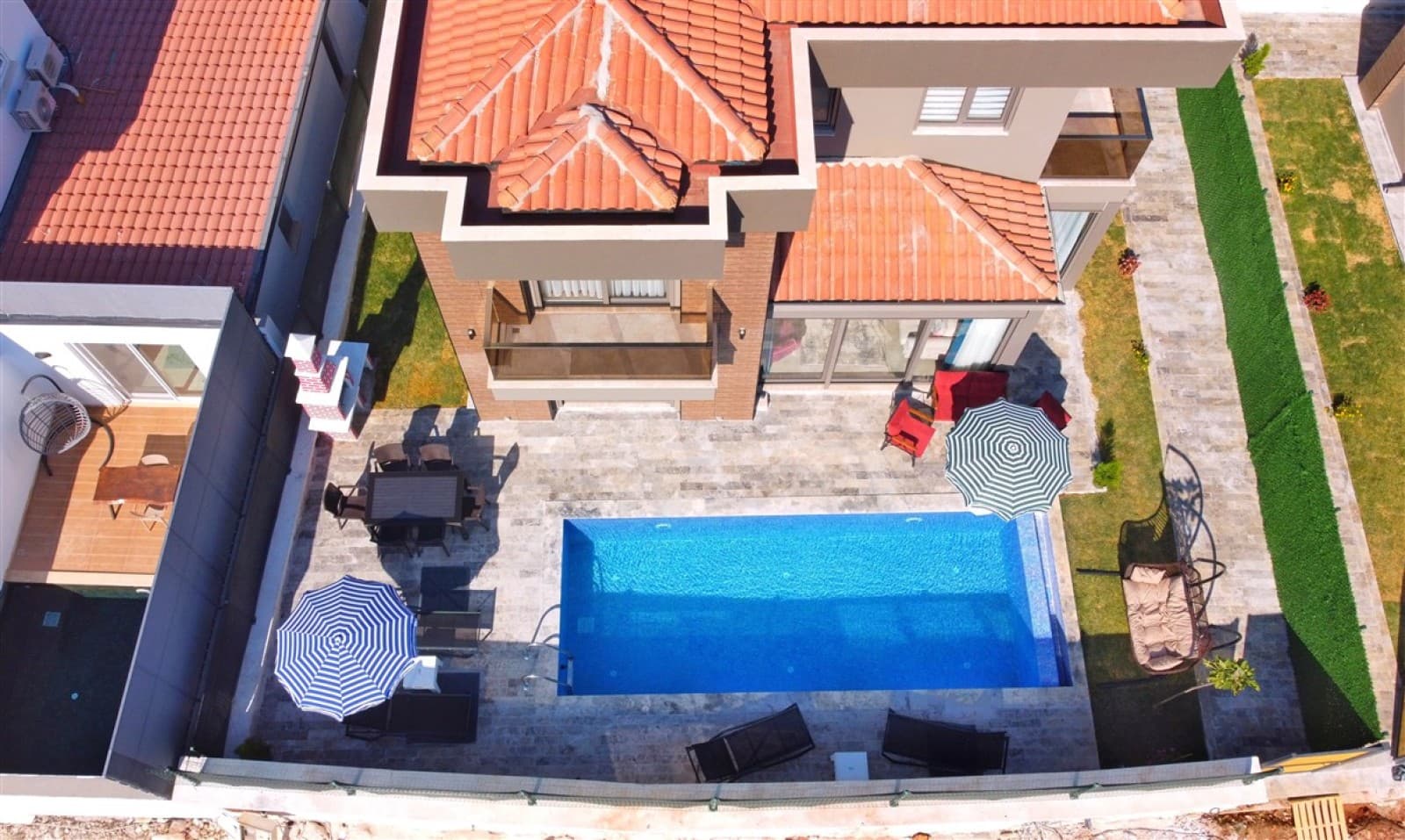 Havuz ve şemsiyeli terası gösteren yüksekten çekilmiş villa dış cephe açısı.