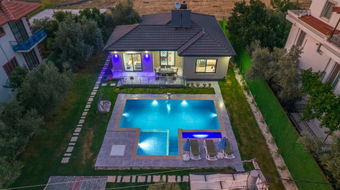 Bahçesinde aydınlatmalı havuz, şezlonglar ve veranda bulunan tek katlı müstakil villa.
