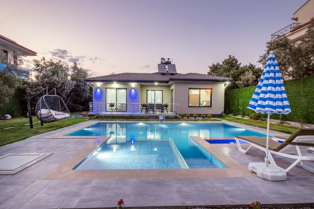 Gün batımında havuzlu müstakil tek katlı villa, salıncak ve şezlong.
