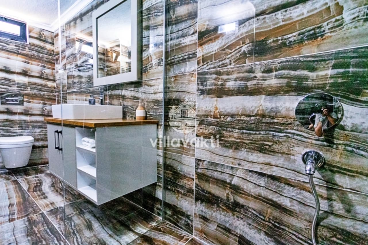 Kahverengi ve beyaz desenli mermer kaplı banyo, duş alanı ve lavabo.
