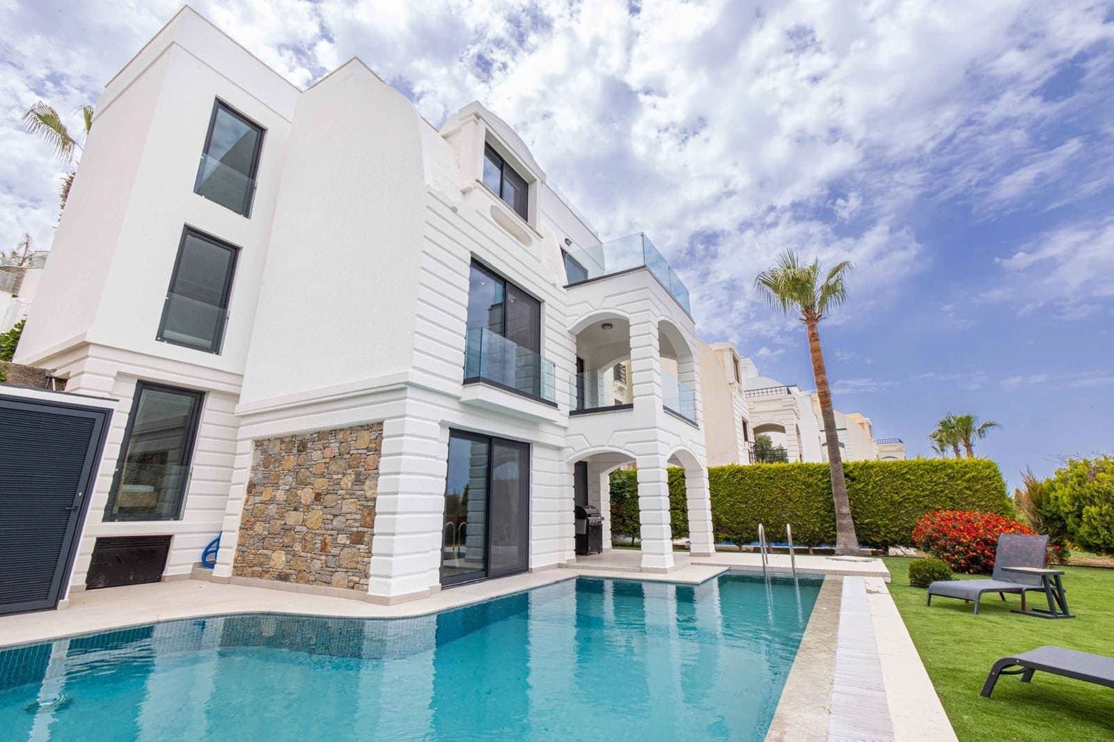 Beyaz dış cepheli, özel havuzlu ve bahçesinde şezlonglar bulunan modern villa.