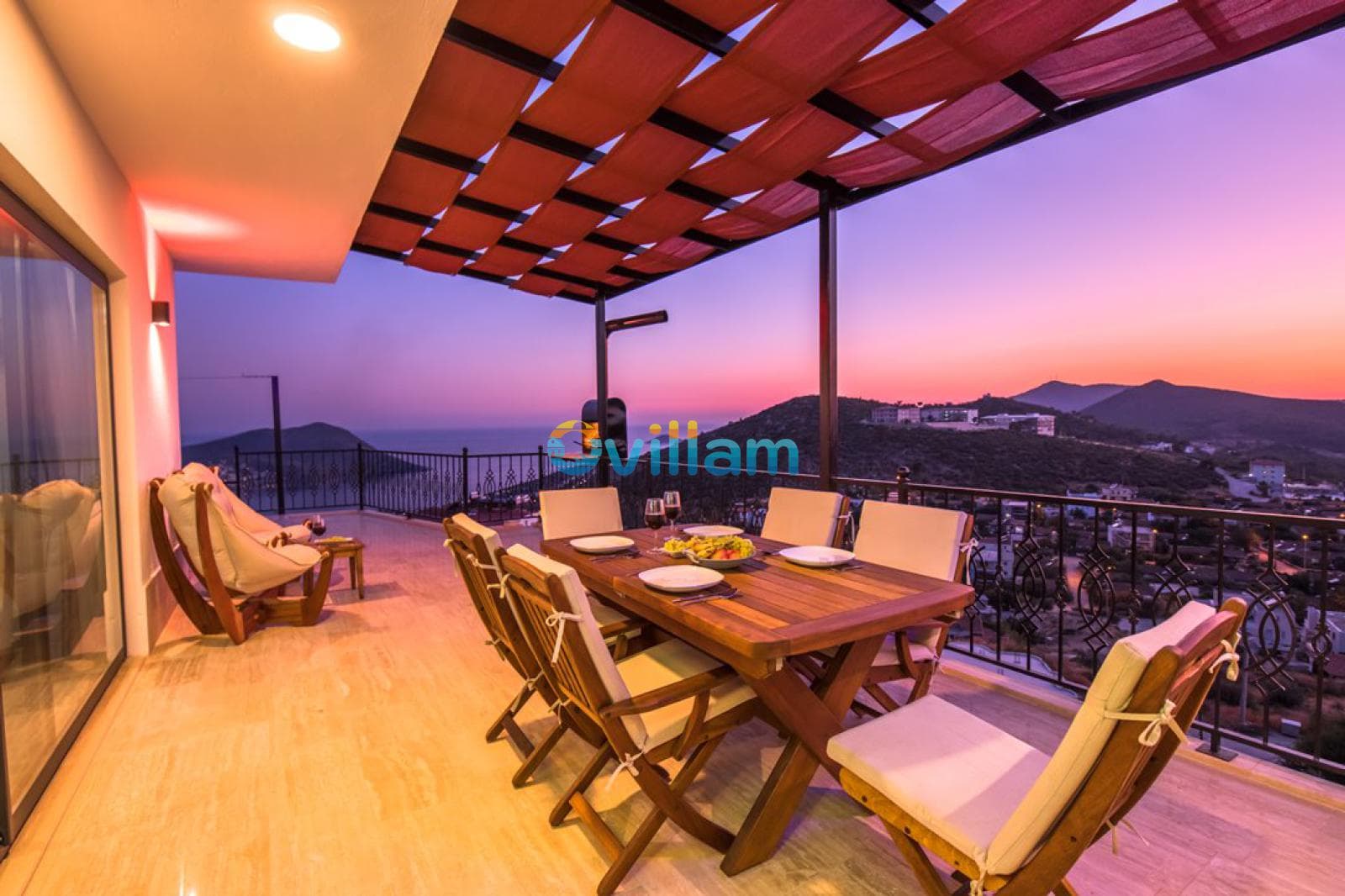 Gün batımında havuz terasında yemek masası, sandalyeler ve deniz manzaralı balkon.