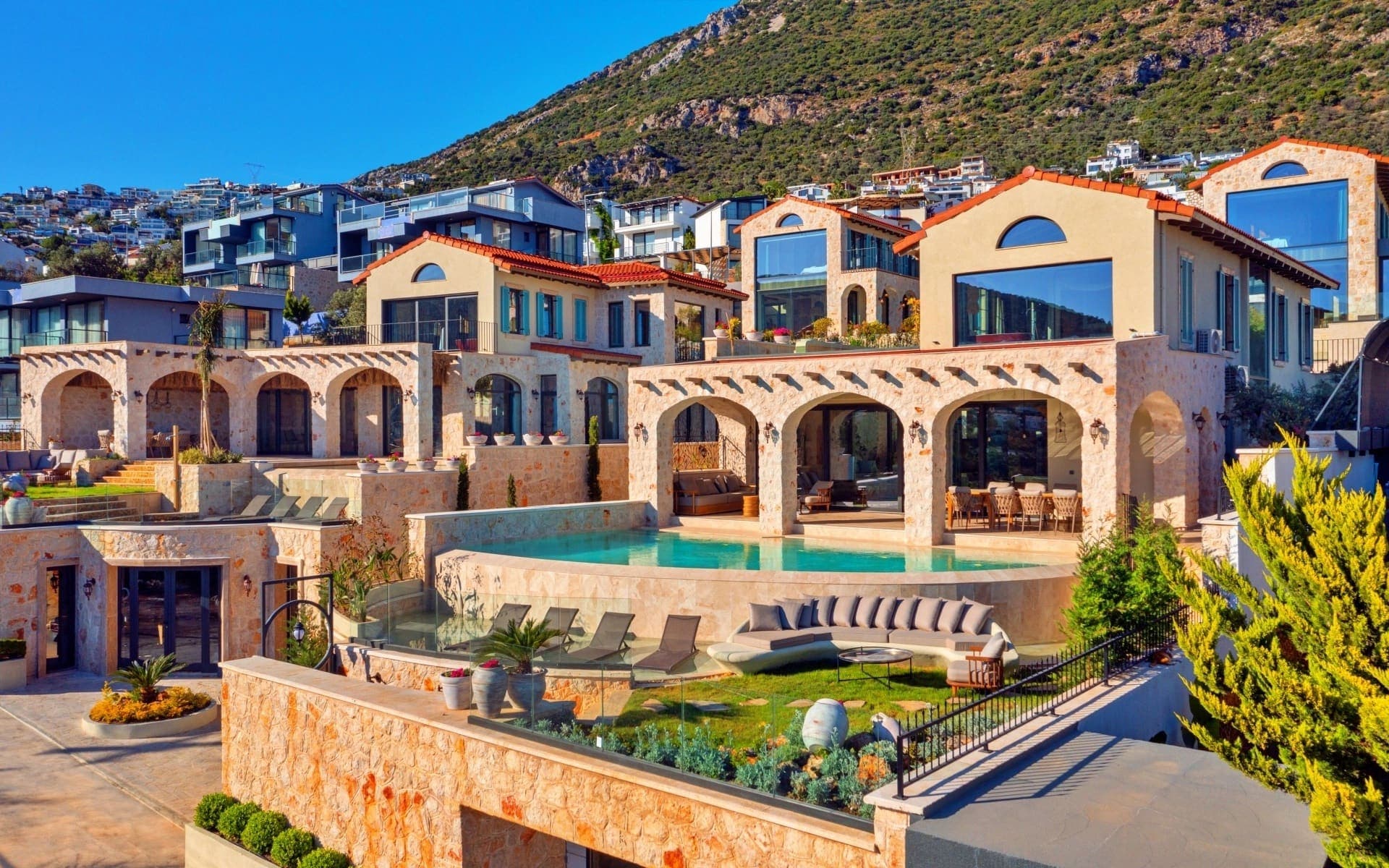 Taş kaplamalı dış cepheye sahip, önünde havuz ve oturma grubu bulunan çok katlı villa.