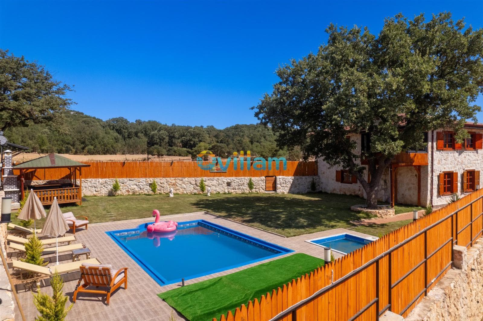 Bahçesinde havuz, şezlonglar, çardak ve pembe flamingo deniz yatağı bulunan taş villa.