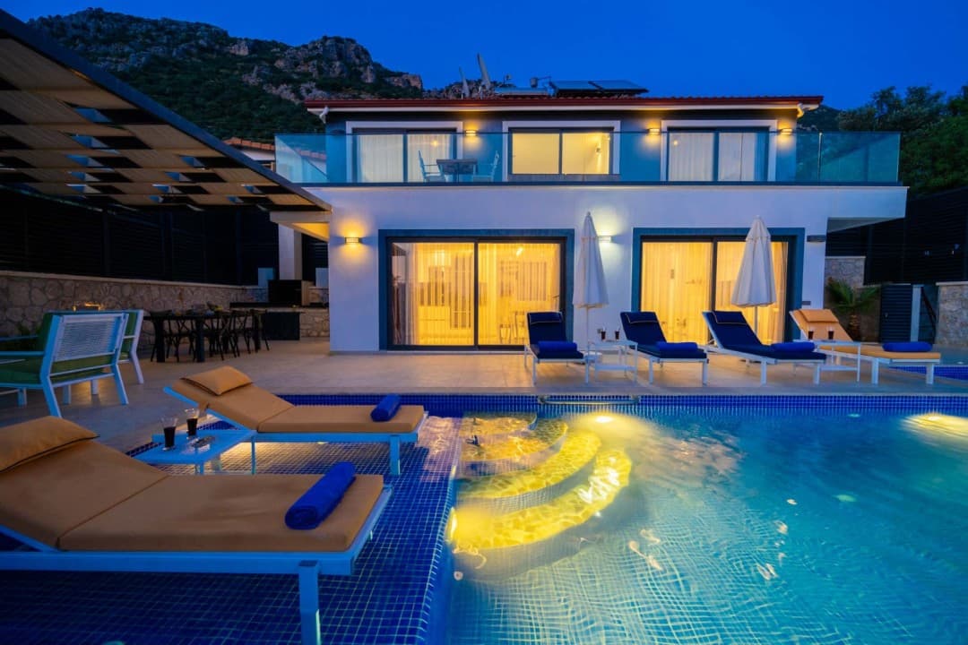 Akşam vakti havuz başı şezlongları ve ışıklandırılmış iki katlı villa.