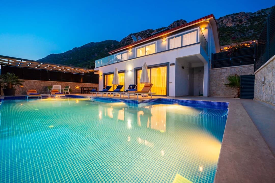 Akşam karanlığında havuz kenarında şezlonglar bulunan iki katlı villa.