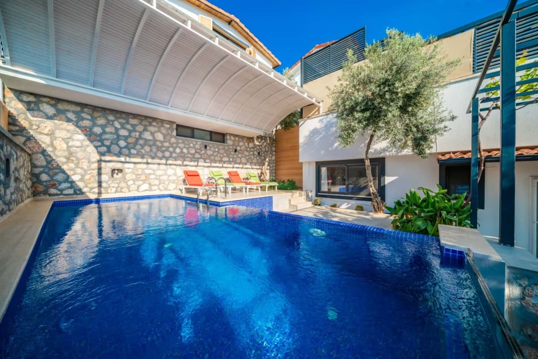 Taş duvarlı, gölgelikli ve şezlonglu özel yüzme havuzu bulunan villa bahçesi.