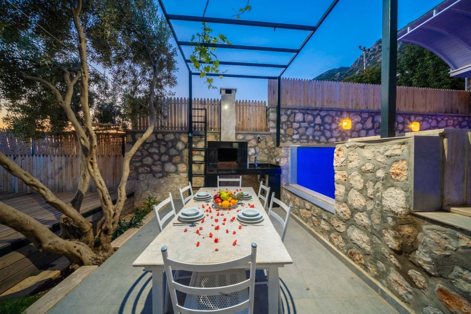 Ahşap tavanlı, taş duvarlı ve barbekülü veranda alanında uzun yemek masası.