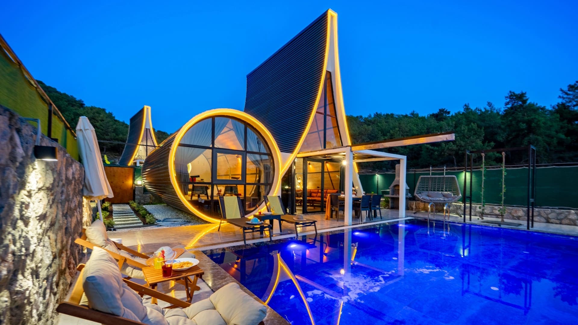 Gece aydınlatmalı özel yüzme havuzu ve sarı ışıklarla süslenmiş modern tasarımlı villa.