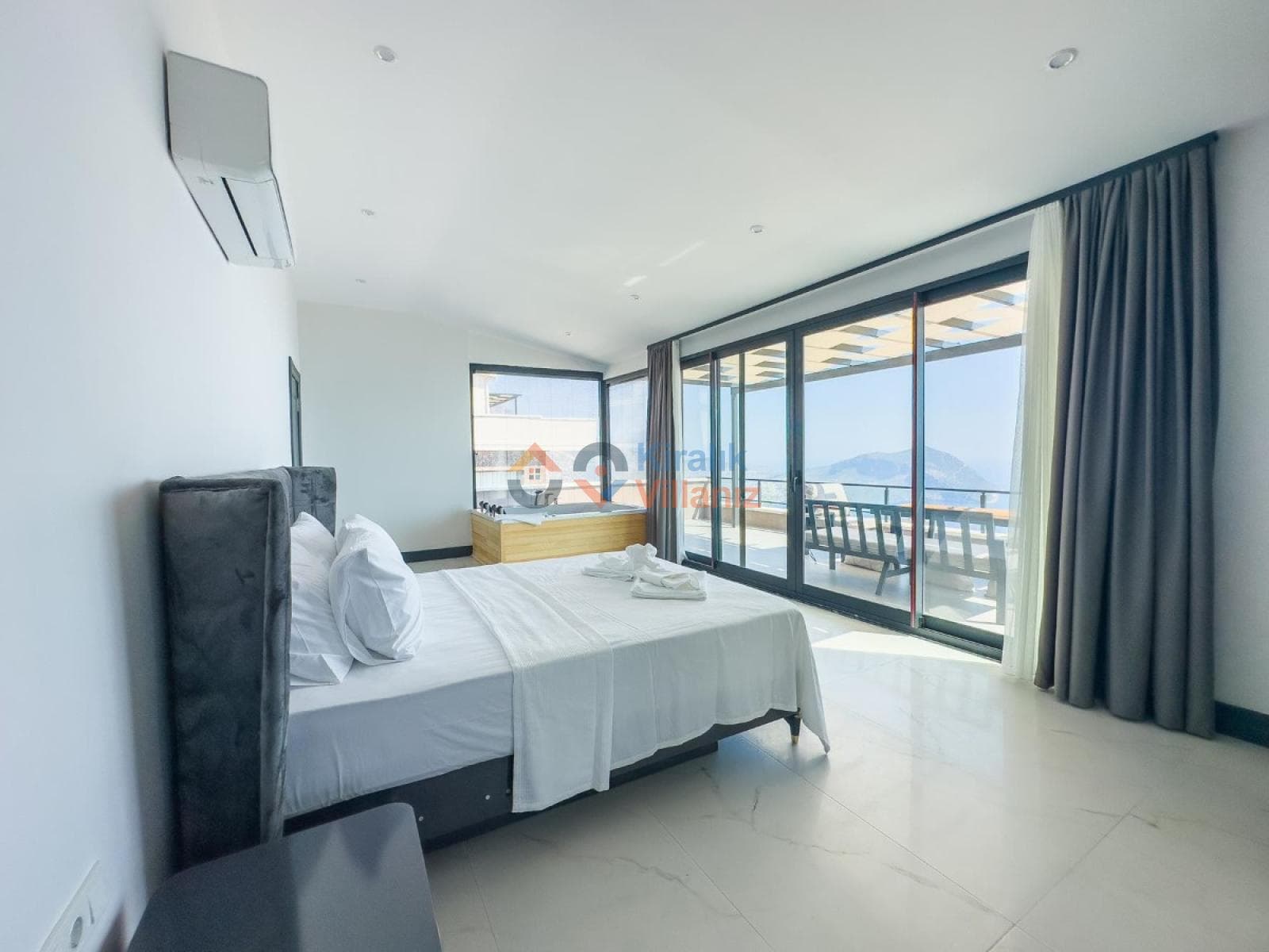 Beyaz yataklı, jakuzili ve geniş cam balkon kapılı modern yatak odası.