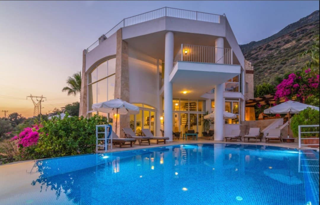 Akşam vakti aydınlatılmış havuzu ve şezlongları olan iki katlı modern villa.