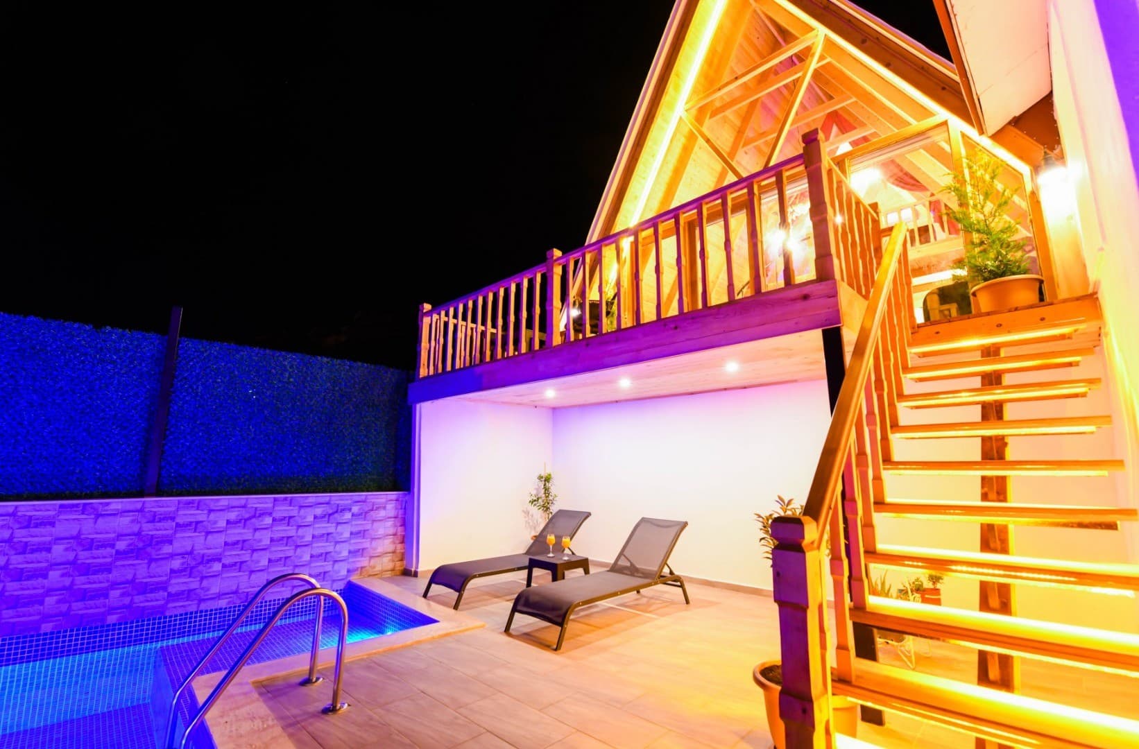 Gecenin karanlığında aydınlatılmış ahşap villa, havuz, şezlonglar ve merdivenler.