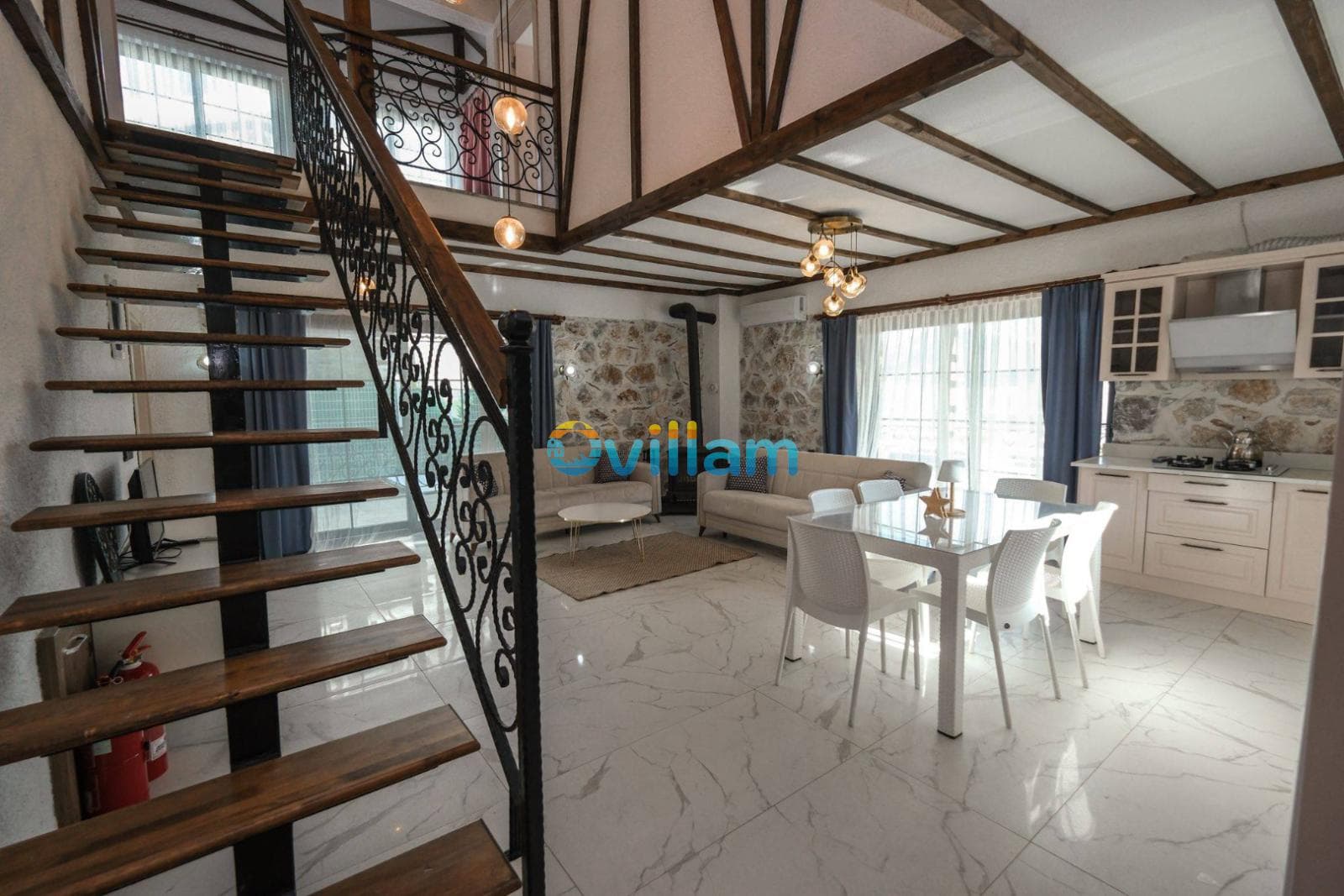 Ahşap merdivenli, açık mutfaklı, beyaz mermer zeminli ve oturma grubu içeren geniş salon.