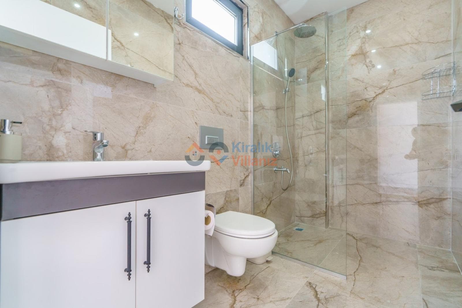 Bej mermer kaplı, cam duşakabinli, beyaz lavabo dolaplı modern banyo.